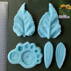 Op de afbeelding: Een set van zes blauwe siliconen mallen voor het maken van zonnebloemdecoraties. De mallen omvatten twee grote bladeren, twee kleinere bladeren en twee bloemcentrum mallen.