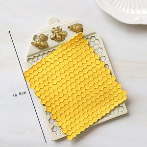 May include: A white silicone mold with a honeycomb pattern and three bee-shaped molds. The mold is 18.8 cm tall.