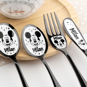 May include: Black and white Mickey Mouse themed children's cutlery set with the name Milan on each piece. The set includes a spoon, fork, and knife.