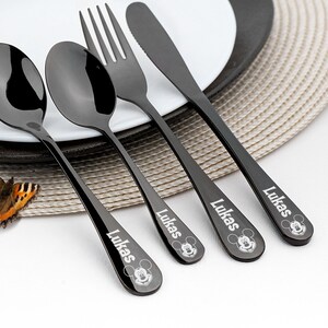 May include: Black cutlery set with Mickey Mouse and the name "Lukas" engraved on each piece. The set includes a fork, knife, and two spoons.