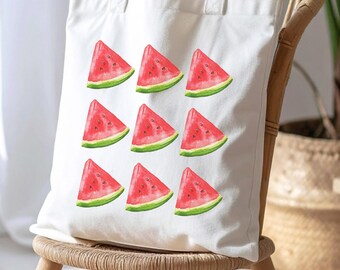 May include: A white canvas tote bag featuring a repeating pattern of watercolor watermelon slices. The tote bag is sitting on a wooden chair with a woven seat. The watermelon slices are red with green rinds.