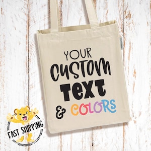 May include: A cream-colored tote bag with the text "YOUR CUSTOM TEXT & COLORS" in black, orange, pink, blue, and purple. The bag has two cream-colored handles and a "Fast Shipping" logo.