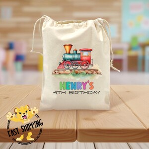 May include: A white cotton drawstring bag with a colorful illustration of a train and the text "HENRY'S 4TH BIRTHDAY".