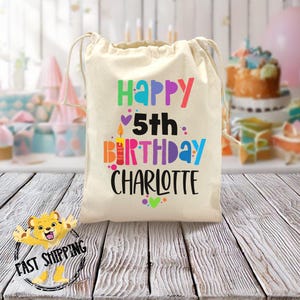 May include: A white cotton drawstring bag with the text "Happy 5th Birthday Charlotte" in colorful letters. The bag is decorated with hearts and confetti.