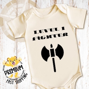 May include: A cream-colored baby onesie with black text that reads "Level 1 Fighter" and a black axe graphic.