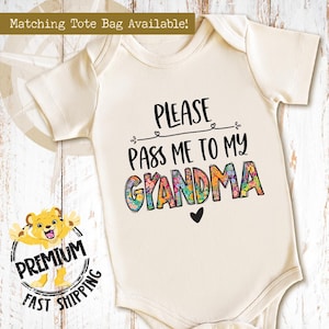 May include: A white baby bodysuit with the text "Please pass me to my Grandma" in colorful letters with a floral design.