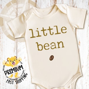 May include: A cream-colored baby onesie with the text "little bean" in brown lettering and a brown coffee bean graphic.