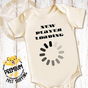 May include: A white baby onesie with black text that reads "NEW PLAYER LOADING" and a black and gray loading circle graphic.