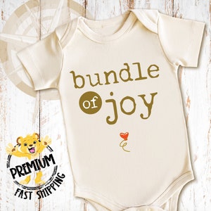 May include: A white baby onesie with a gold graphic that says "bundle of joy" with a small red heart balloon.