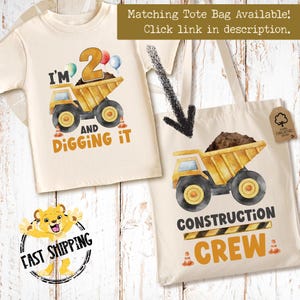 May include: A cream-colored t-shirt and a matching tote bag, both featuring a yellow dump truck graphic. The t-shirt displays the text I'M 2 AND DIGGING IT with balloons. The tote bag features the text CONSTRUCTION CREW and a brown tag.