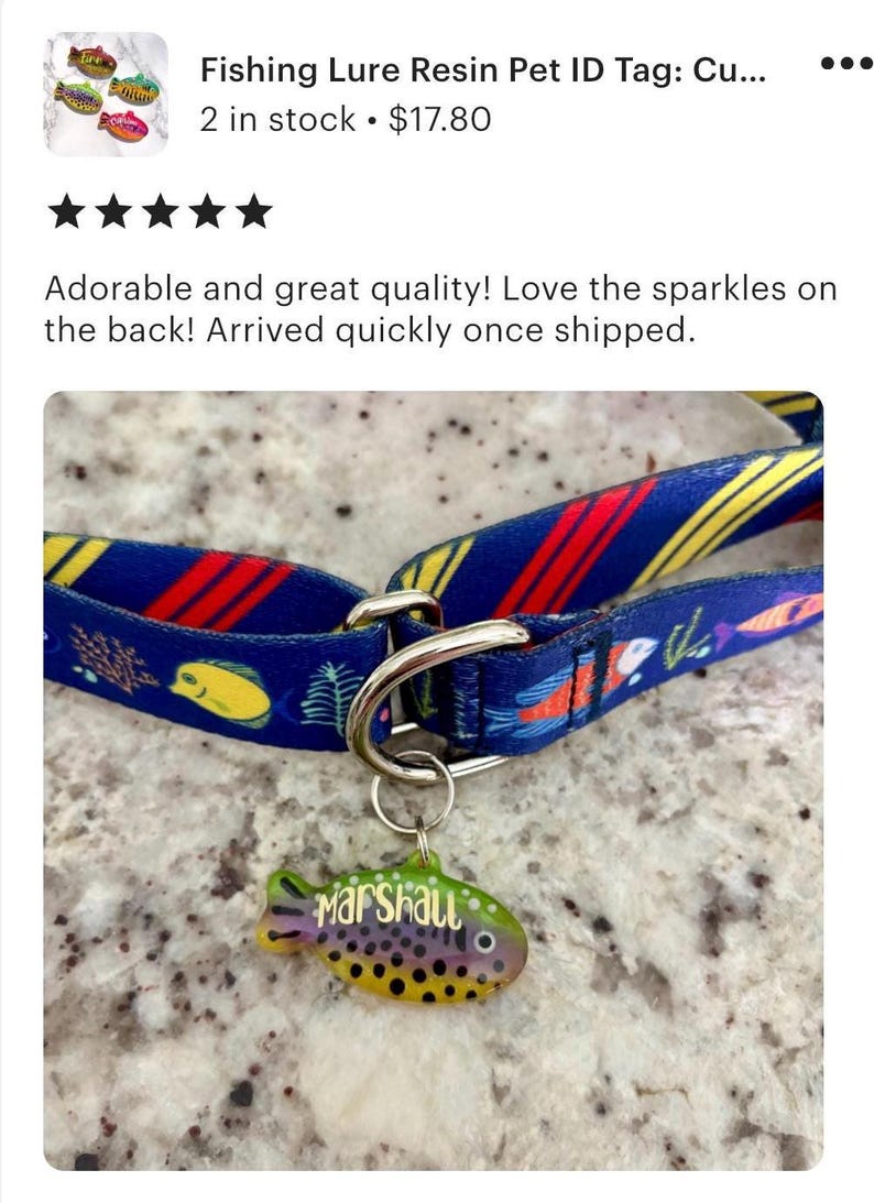 Pu&ograve; includere: Un collare per cani con un motivo blu e giallo, un anello in metallo argentato e un'etichetta identificativa per animali a forma di pesce. L'etichetta &egrave; verde, gialla e viola con il nome "Marshall".