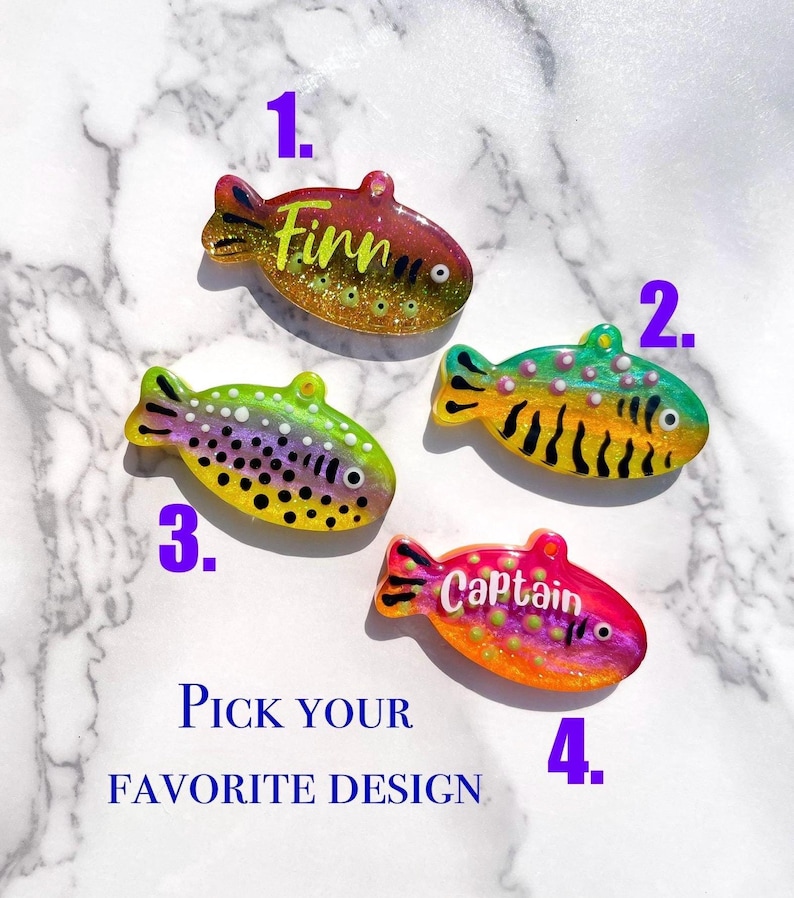 Pu&ograve; includere: Quattro ciondoli in resina a forma di pesce con accenti glitterati. Ogni ciondolo ha un design unico, inclusi nomi come "Finn" e "Captain". &Egrave; presente anche il testo "Pick your favorite design". Questi ciondoli sono probabilmente per gioielli o artigianato.
