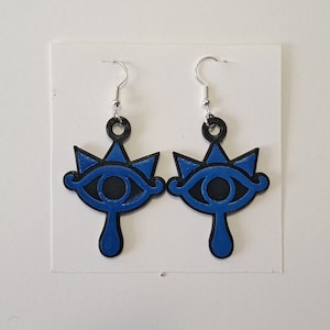 May include: A pair of blue and black earrings featuring a stylized eye design. The earrings are hanging from silver hooks.