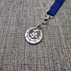 May include: A silver key chain with a black and white circular charm featuring a Japanese character. The charm is attached to a blue lanyard.
