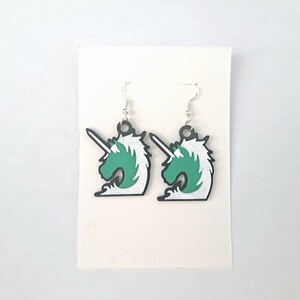 May include: A pair of silver earrings with green and white unicorn head charms. The unicorn head is a stylized design with a horn and mane.