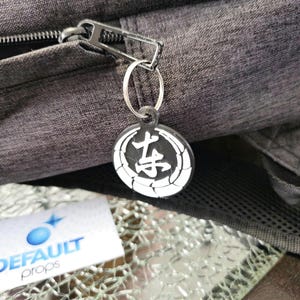 May include: A black zipper pull with a silver ring and a black and white round keychain with Japanese characters. The keychain has a white circle with a black kanji character in the center and a white circle around the kanji character.