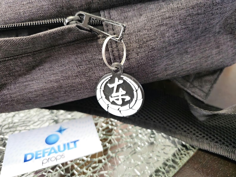 May include: A black zipper pull with a silver ring and a black and white round keychain with Japanese characters. The keychain has a white circle with a black kanji character in the center and a white circle around the kanji character.