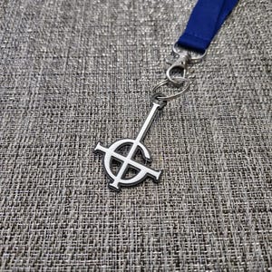 May include: A silver-coloured keychain with a white inverted pentagram symbol. The keychain is attached to a blue lanyard.