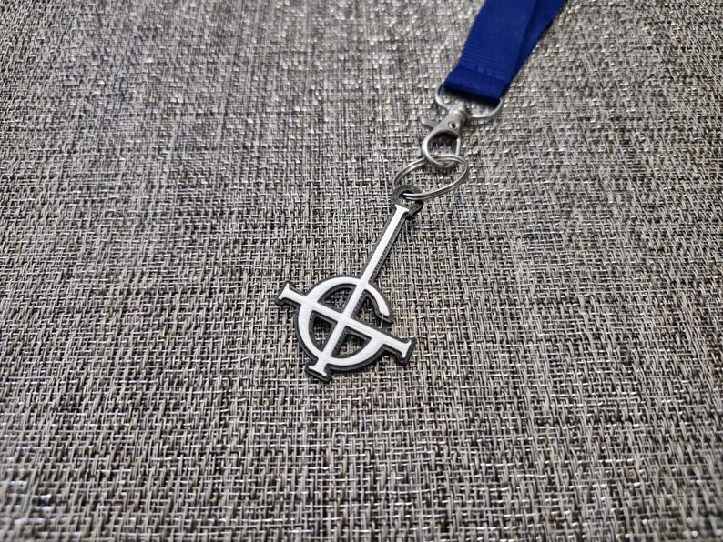 May include: A silver-coloured keychain with a white inverted pentagram symbol. The keychain is attached to a blue lanyard.