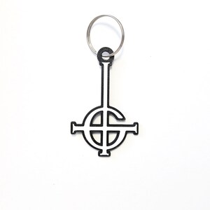 May include: Black and white metal keychain featuring the inverted pentagram symbol, also known as the upside-down cross.