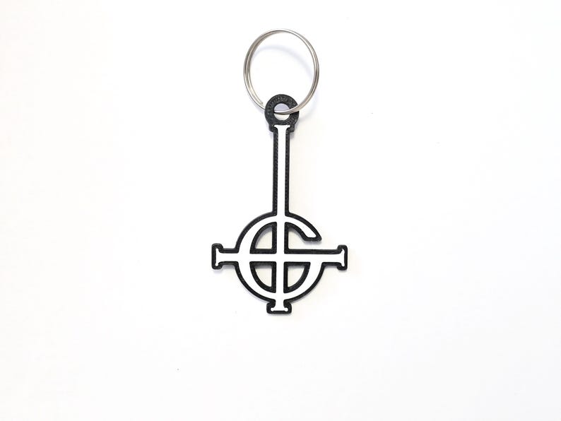 May include: Black and white metal keychain featuring the inverted pentagram symbol, also known as the upside-down cross.