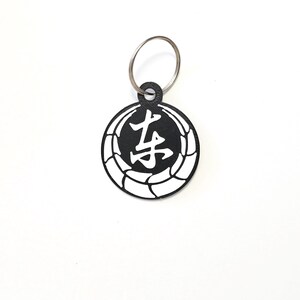 May include: Black and white keychain with a circle design featuring a Japanese character in the center. The character is "老" which means "old" or "elder".