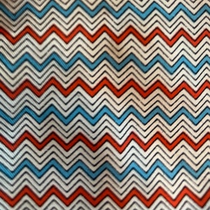 Puede incluir: Una tela blanca con un patrón de chevron rojo, azul y negro.