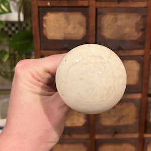 Pode incluir: Um almofariz de cerâmica branca com uma superfície lisa e arredondada. O almofariz está sendo segurado por uma mão.