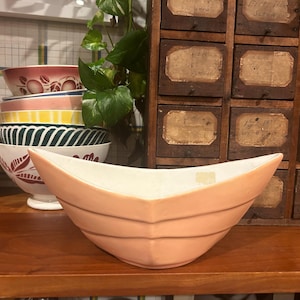 Op de afbeelding: Een brede, ondiepe serveerschaal van lichtroze keramiek met een licht gebogen rand. De schaal heeft drie horizontale ribbels aan de buitenkant.