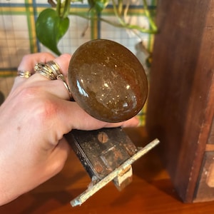 May include: A close-up of a brown, round door knob with a metal latch. The knob is made of a smooth, polished material.