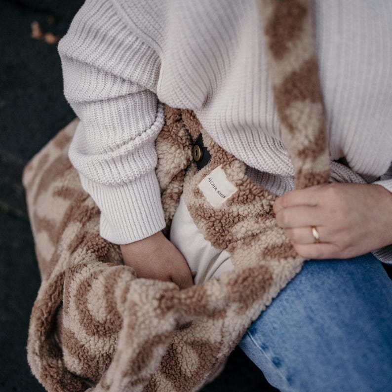 Puede incluir: Una bolsa de mano de color marr&oacute;n y beige peluda con una etiqueta blanca que dice "Aloha Kids".