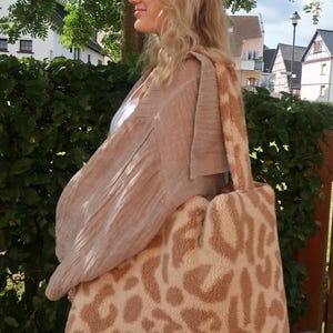 Puede incluir: Un bolso tote grande de color crema con estampado de leopardo marr&oacute;n. El bolso tiene una textura suave y esponjosa.