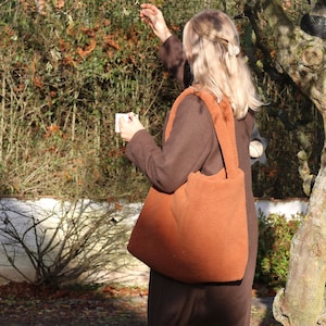 Puede incluir: Un bolso tote de color marr&oacute;n peludo con asas largas. El bolso lo lleva una persona con el pelo largo y rubio.