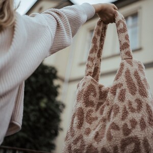 Puede incluir: Una bolsa de mano de color marr&oacute;n y blanco con un dise&ntilde;o de estampado de leopardo. La bolsa tiene dos asas y la est&aacute; sujetando una persona.