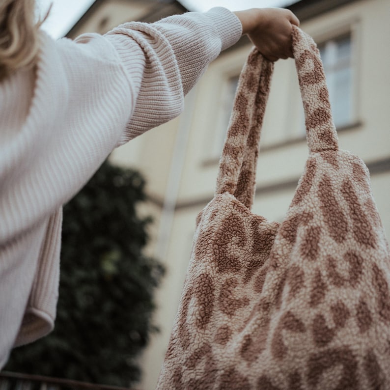 Puede incluir: Una bolsa de mano de color marr&oacute;n y blanco con un dise&ntilde;o de estampado de leopardo. La bolsa tiene dos asas y la est&aacute; sujetando una persona.