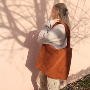 Puede incluir: Una bolsa de mano de color marr&oacute;n peluda con una correa larga. La bolsa la lleva una persona que lleva un su&eacute;ter marr&oacute;n claro y pantalones beige.