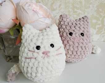 May include: Two crocheted cat toys, one white and one pink. The white cat has black eyes and a pink nose. The pink cat has black eyes and a pink nose. Both cats have a crocheted texture.