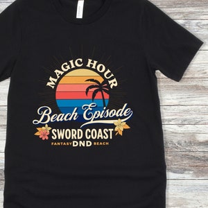 Pode incluir: Camiseta preta com um gr&aacute;fico de p&ocirc;r do sol retr&ocirc; e o texto "Magic Hour Beach Episode Sword Coast Fantasy DND Beach".