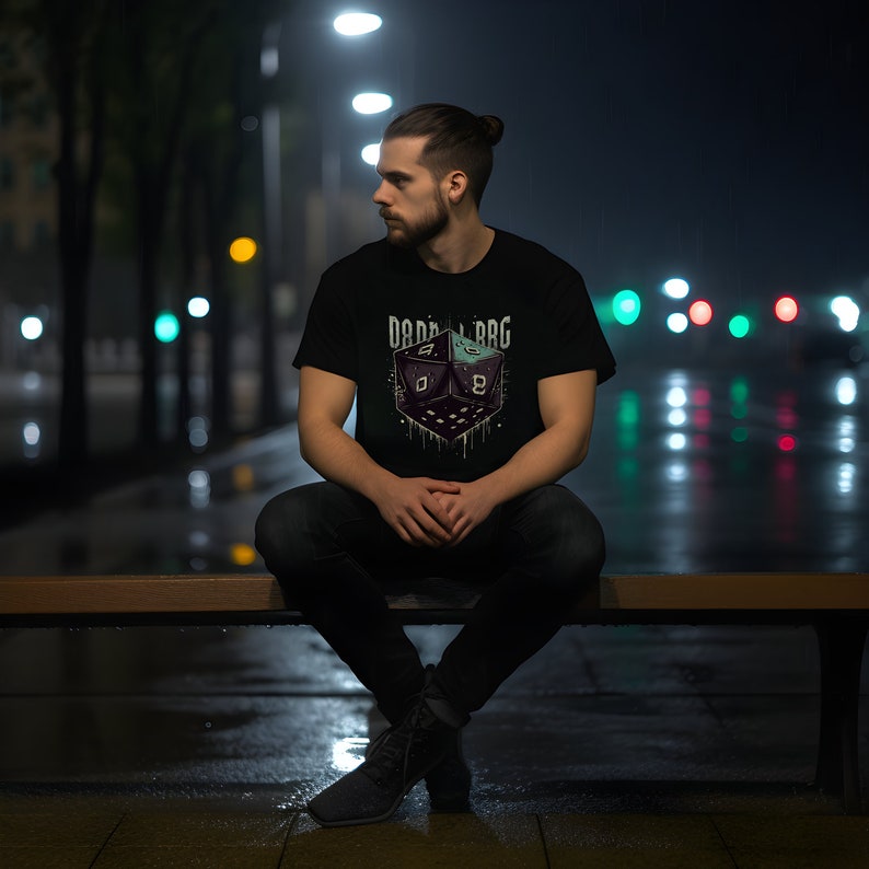 Op de afbeelding: Een zwart T-shirt met een afbeelding van een groene en zwarte dobbelsteen met de tekst "D&D LBRG" gedrukt op de voorkant.