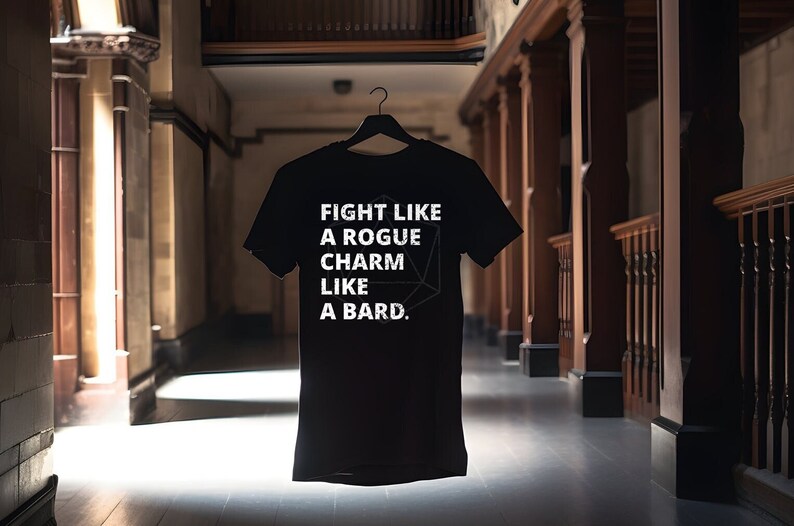 May include: Black t-shirt with white text that reads "Fight like a rogue, charm like a bard." A white geometric shape is behind the text.