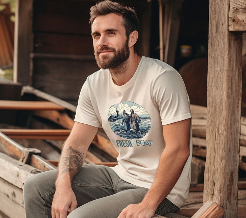 K&ouml;nnte beinhalten: Ein wei&szlig;es T-Shirt mit einer blauen und wei&szlig;en Illustration von zwei Personen in einem Boot. Der Text "FRESH BOAT" ist unter der Illustration aufgedruckt.