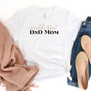May include: White t-shirt with the text "World's Best DND Mom" in black and brown lettering.