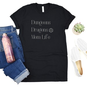 May include: Black t-shirt with white text that reads "Dungeons Dragons Mom Life" and a white Dungeons and Dragons dice symbol.