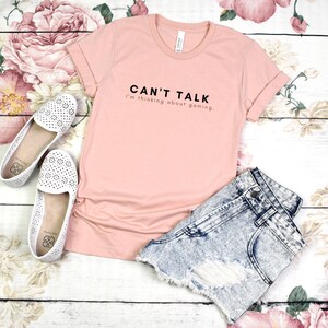 K&ouml;nnte beinhalten: Ein rosa T-Shirt mit dem Aufdruck "Can't Talk I'm thinking about gaming." auf der Vorderseite.
