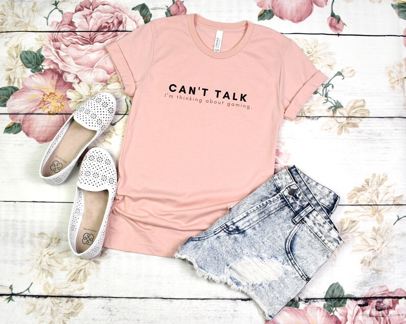 K&ouml;nnte beinhalten: Ein rosa T-Shirt mit dem Aufdruck "Can't Talk I'm thinking about gaming." auf der Vorderseite.