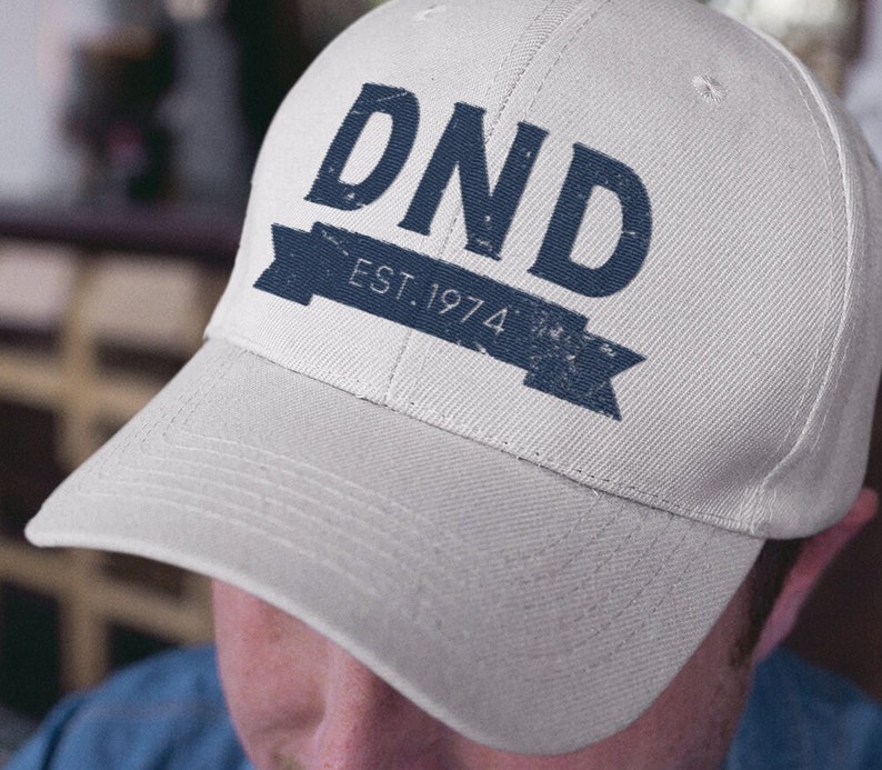 A close-up of a dad hat with DND "Est. 1974" a DnD-related quote