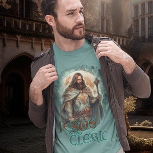 May include: A light blue t-shirt with a graphic of a man in armor holding a staff. The text "Jesus is my Cleric" is printed on the shirt.