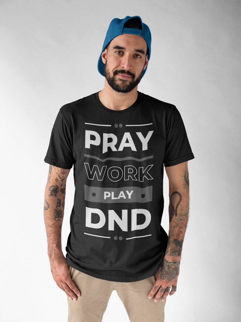 K&ouml;nnte beinhalten: Ein schwarzes T-Shirt mit dem Aufdruck "Pray Work Play DND" in wei&szlig; auf der Vorderseite.