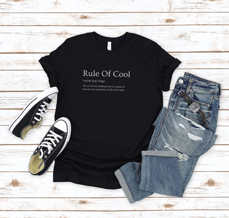 May include: Black t-shirt with white text that reads "Rule Of Cool /rul av kul/ lingo The act of over looking rules in a game to increase the enjoyment of all at the table."
