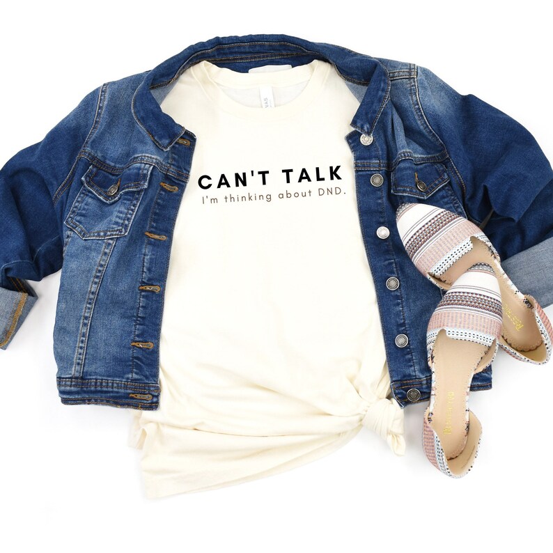 May include: A white t-shirt with the text "CAN'T TALK I'm thinking about DND." printed in black.